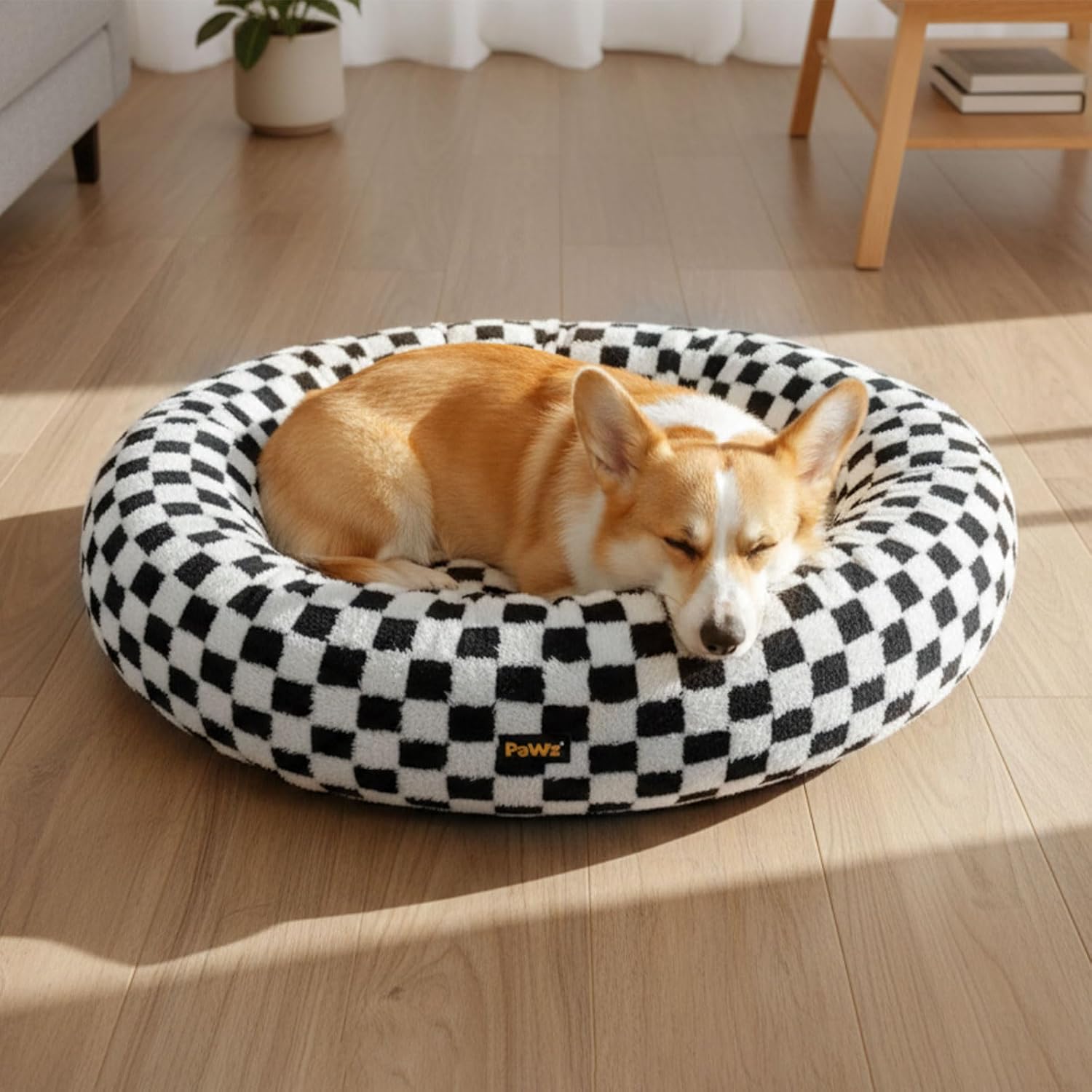 Dog resting on a black and white checkered pet bed in a room with wooden flooring at Pet Servo