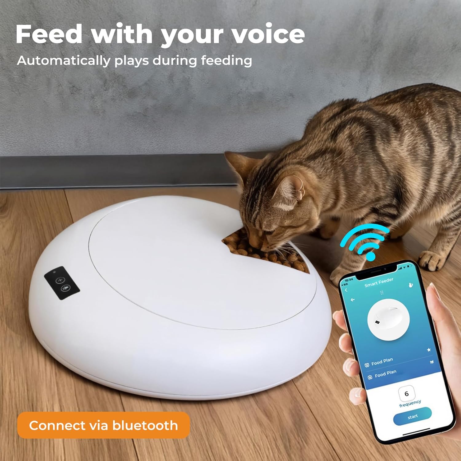 A brown tabby cat is eating from a white robotic pet feeder on a wooden floor, with a hand holding a smartphone showing a companion app interface. Text on the image reads 'Feed with your voice' and 'Connect via Bluetooth' at Pet Servo