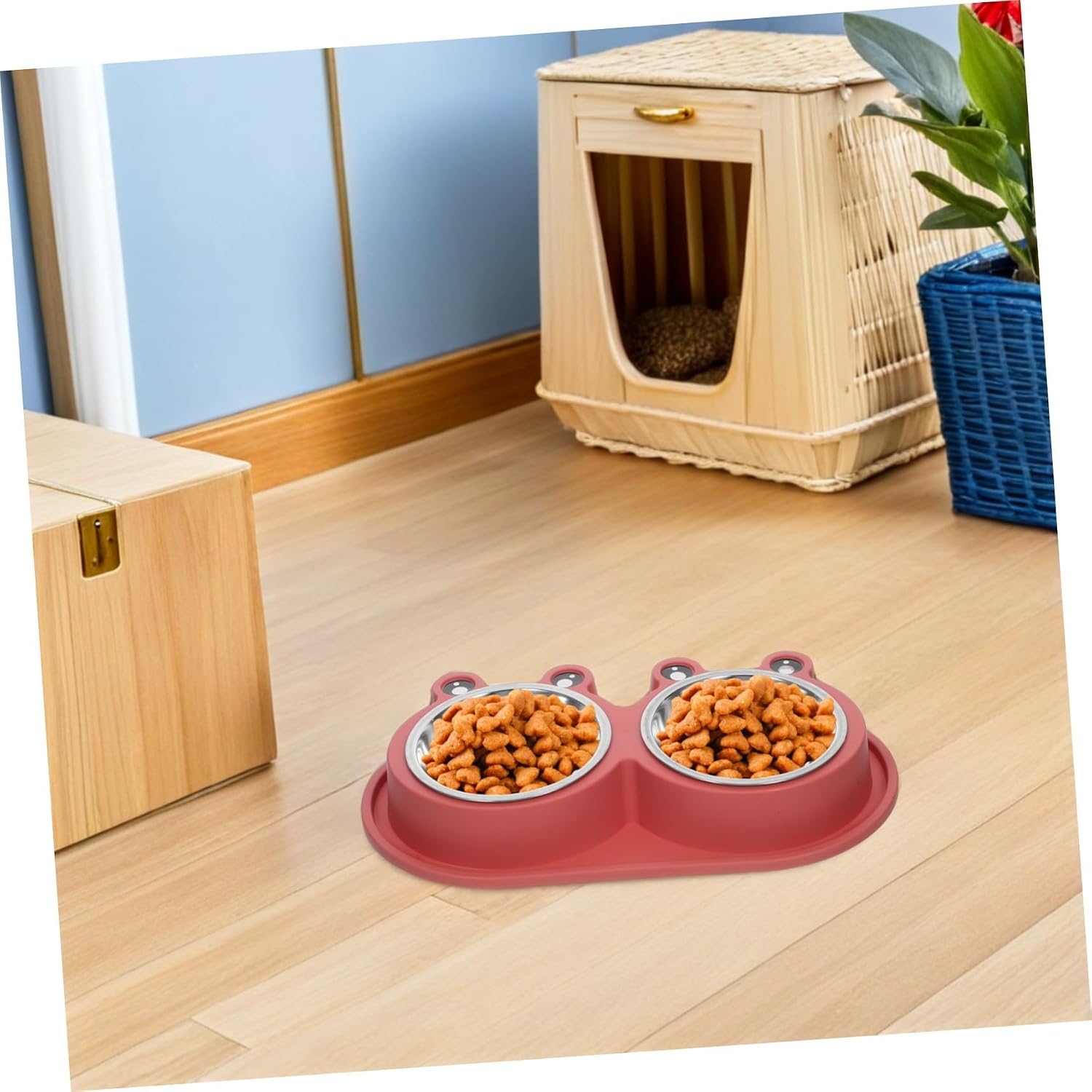 A pink silicone pet feeder and waterer bowl set on a light wood floor, with two stainless steel bowls filled with dry dog food. A wooden pet house and a blue basket with a plant are visible in the background at Pet Servo