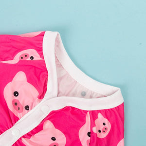 A close-up of a baby garment in bright pink with a repeating cartoon pig print and white trim, laid against a light blue background at Pet Servo