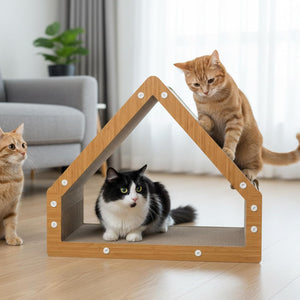A house-shaped cat scratcher with a light wood frame and gray scratching panels, shown in a bright living room with three cats around it at Pet Servo