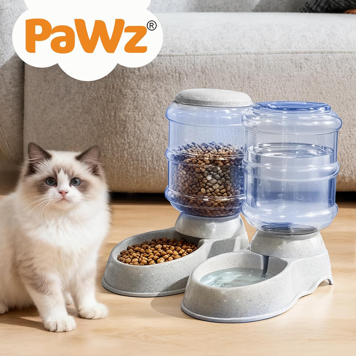 A cat food and water dispenser set shown on a wooden floor in front of a sofa, with a fluffy white cat sitting to the left. The dispenser includes a gray food bowl filled with kibble, a water reservoir filled with water, and a gray water bowl at Pet Servo