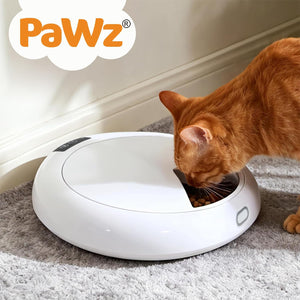 An orange tabby cat eating from a round white robotic pet feeder on a gray carpet, with the Pawz brand logo shown in the top left corner at Pet Servo