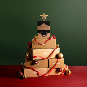 A Christmas-themed gift box tower made of stacked kraft paper boxes, decorated with red ribbons, gold and red ornaments, and topped with a gold star. The top box features a cute cartoon bear face at Pet Servo