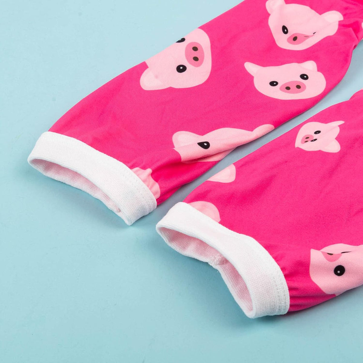 Bright pink fabric sleeves or cuffs with a repeating cartoon pig face print and white ribbed trim, laid on a light blue background at Pet Servo