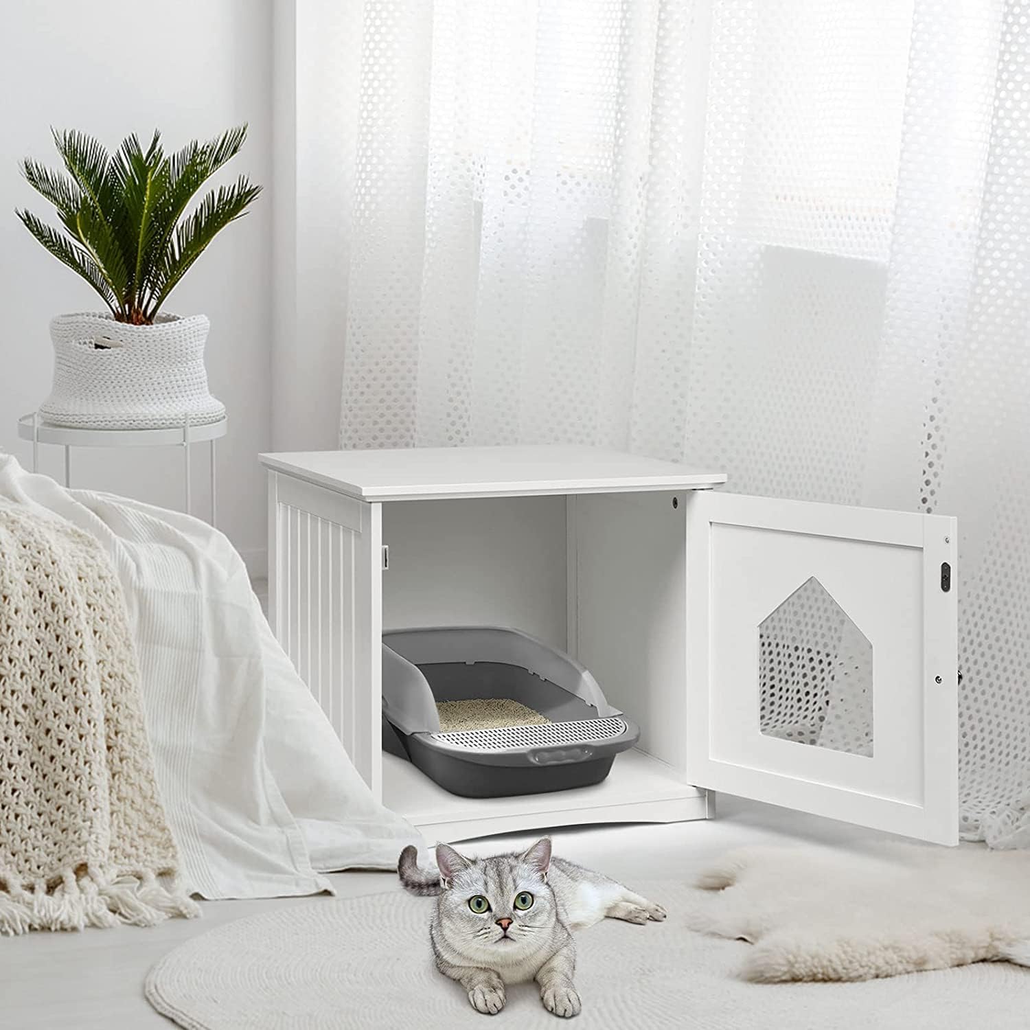 Cat lying on a white floor next to a white pet enclosure with a gray litter box inside, in a bright room at Pet Servo