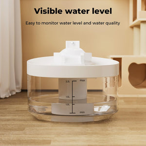 A clear cylindrical water tank with a white lid and internal level indicator, shown on a wooden floor in a home setting. Text at the top reads 'Visible water level' and 'Easy to monitor water level and water quality at Pet Servo