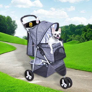 A small white dog sits inside a stroller-style pet stroller with a black-and-white gingham pattern, shown outdoors on a paved path with green grass and trees in the background at Pet Servo