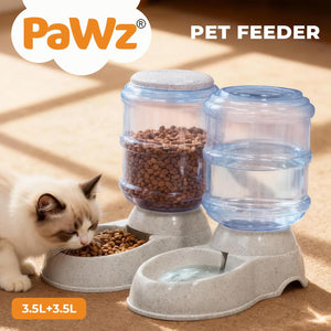 A cat dual automatic feeder and water dispenser set by Pawz, featuring a beige textured base, clear plastic food and water reservoirs filled with kibble and water, and a shallow bowl. A white and brown cat is shown eating from the feeder on a warm beige floor at Pet Servo