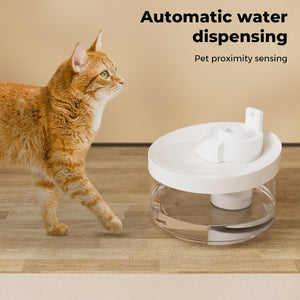 An orange tabby cat walks toward a white and clear pet water dispenser on a wood floor against a beige wall, with text reading 'Automatic water dispensing' and 'Pet proximity sensing' at Pet Servo