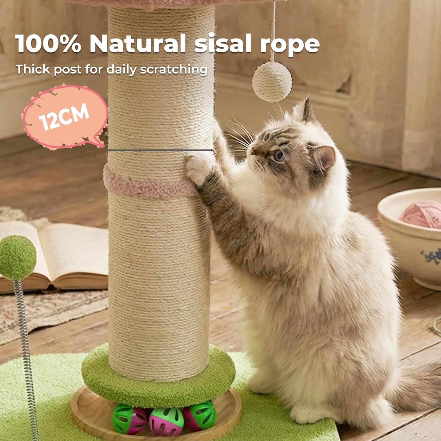 A fluffy cream and gray cat stands beside a tall sisal rope cat tree in a home setting, touching the scratching post. The scene includes promotional text reading '100% Natural sisal rope', 'Thick post for daily scratching', and '12CM', along with a hanging ball toy, a book, and a bowl on a wooden floor at Pet Servo