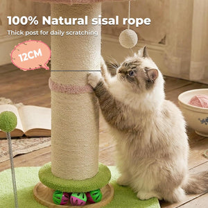 A fluffy cream and gray cat stands beside a tall sisal rope cat tree in a home setting, touching the scratching post. The scene includes promotional text reading '100% Natural sisal rope', 'Thick post for daily scratching', and '12CM', along with a hanging ball toy, a book, and a bowl on a wooden floor at Pet Servo