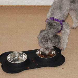 Dog eating from a black and silver double-bowl feeder on a beige floor at Pet Servo
