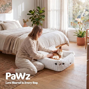 Woman sitting on the floor with a cat on a pet bed in a bright bedroom, featuring the PaWz brand at Pet Servo