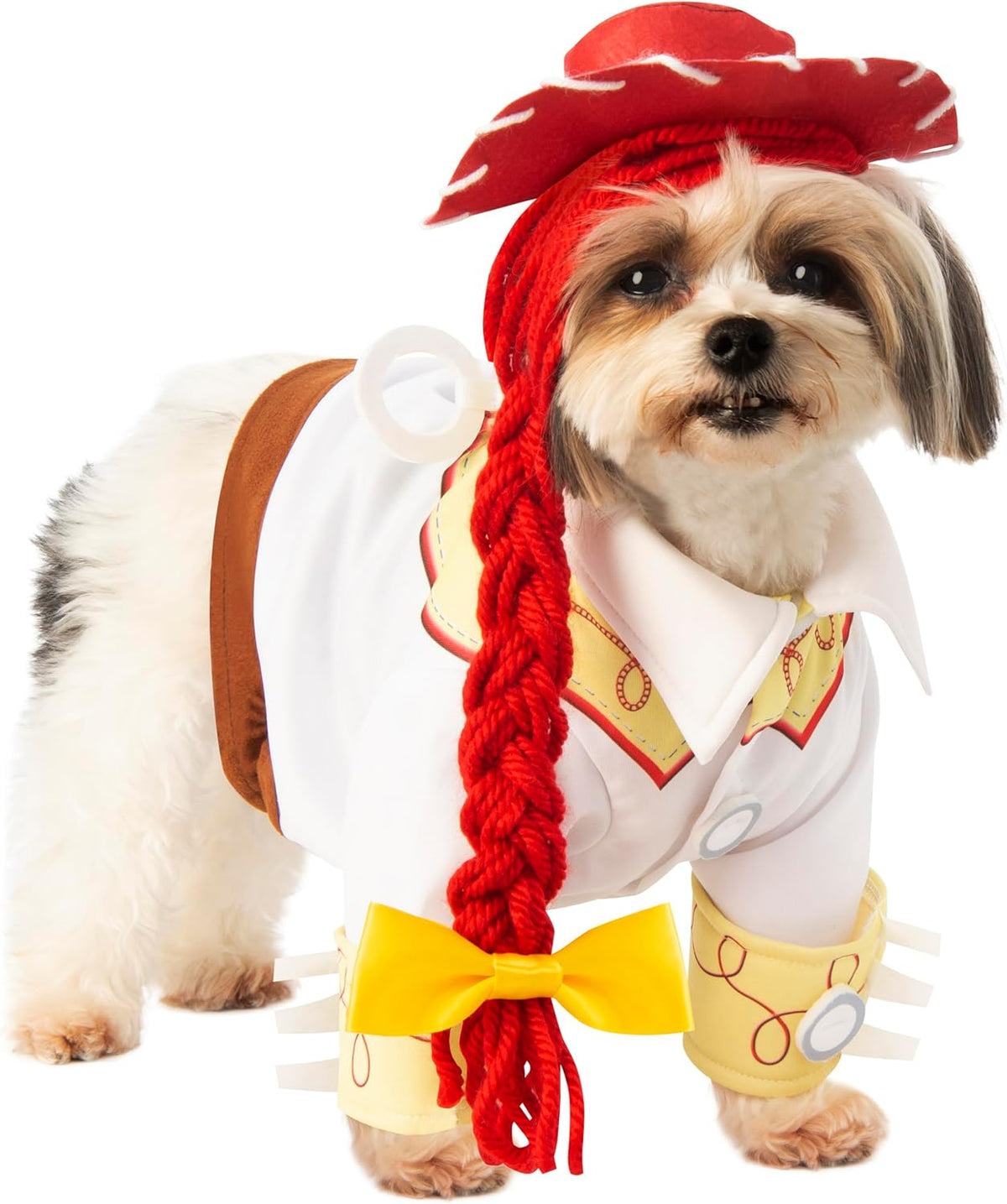 A small Shih Tzu dog wearing a cowboy costume, featuring a white shirt with yellow and red trim, a brown saddle-like back piece, a bright red braided wig, and a red hat, photographed on a white background at Pet Servo