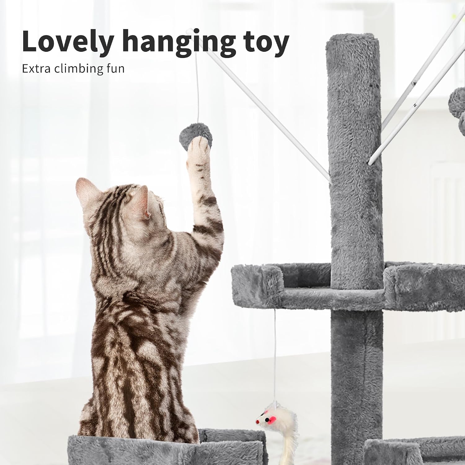 A brown and gray tabby cat stands on its hind legs, reaching up to play with a hanging toy attached to a gray plush cat tree. The scene is brightly lit with text reading 'Lovely hanging toy' and 'Extra climbing fun' at the top at Pet Servo