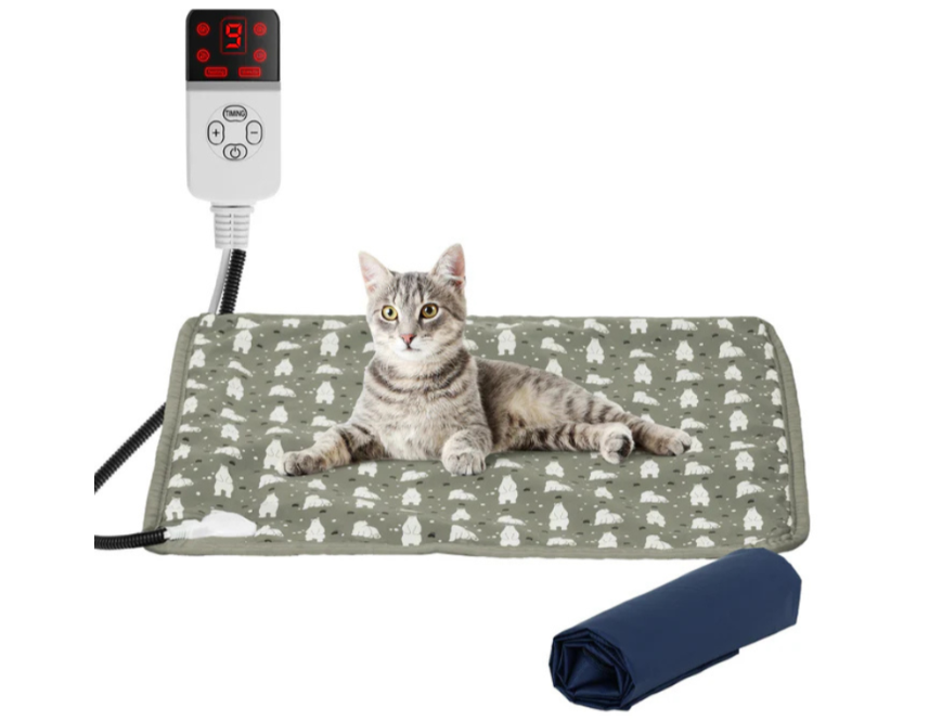 Cat lying on a patterned heating pad with a digital temperature controller and folded towel on a white background