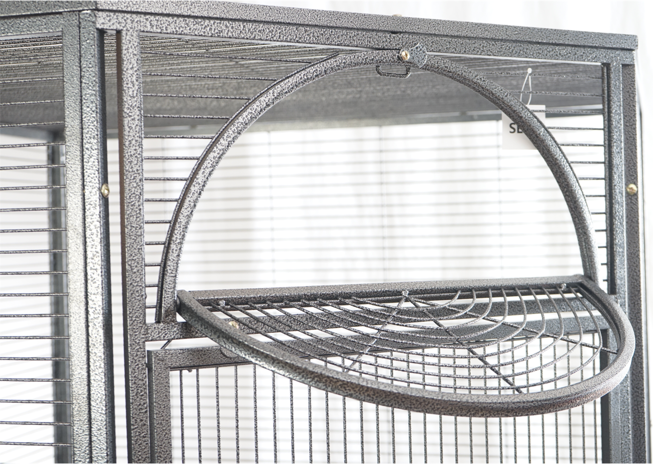 Bird cage with a round perch inside, against a window background at Pet Servo