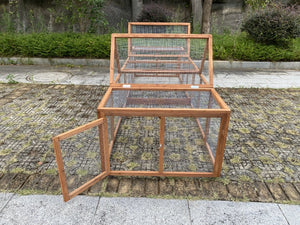 A wooden rabbit hutch with wire mesh panels, featuring a hinged door on the left side that is open, set outdoors on a paved stone surface with greenery in the background at Pet Servo