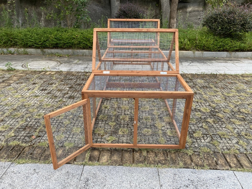 A wooden rabbit hutch with wire mesh panels, featuring a hinged door on the left side that is open, set outdoors on a paved stone surface with greenery in the background at Pet Servo