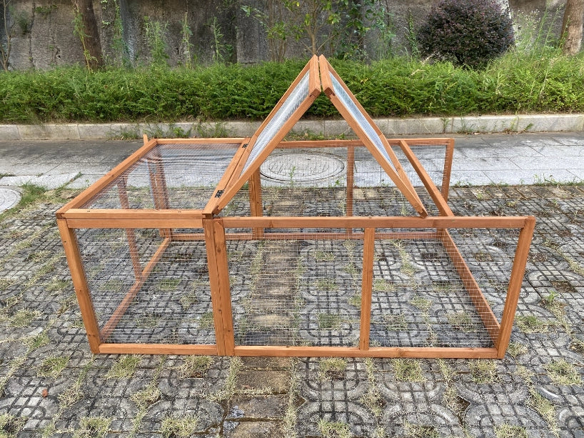 A wooden chicken coop or small greenhouse with wire mesh panels, photographed outdoors on a paved stone surface with grass and shrubs in the background at Pet Servo