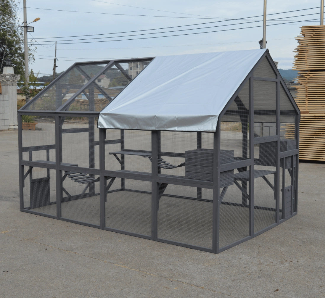 A gray metal greenhouse with a white roof cover, situated outdoors on a concrete surface with a stack of wooden boards in the background at Pet Servo