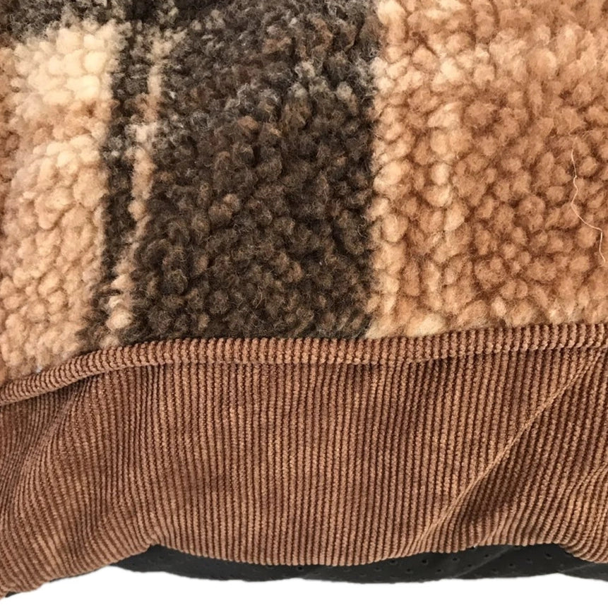 Close-up of a plush sherpa-style cushion cover with vertical stripes in beige, brown, and dark brown, finished with a brown corduroy trim at Pet Servo