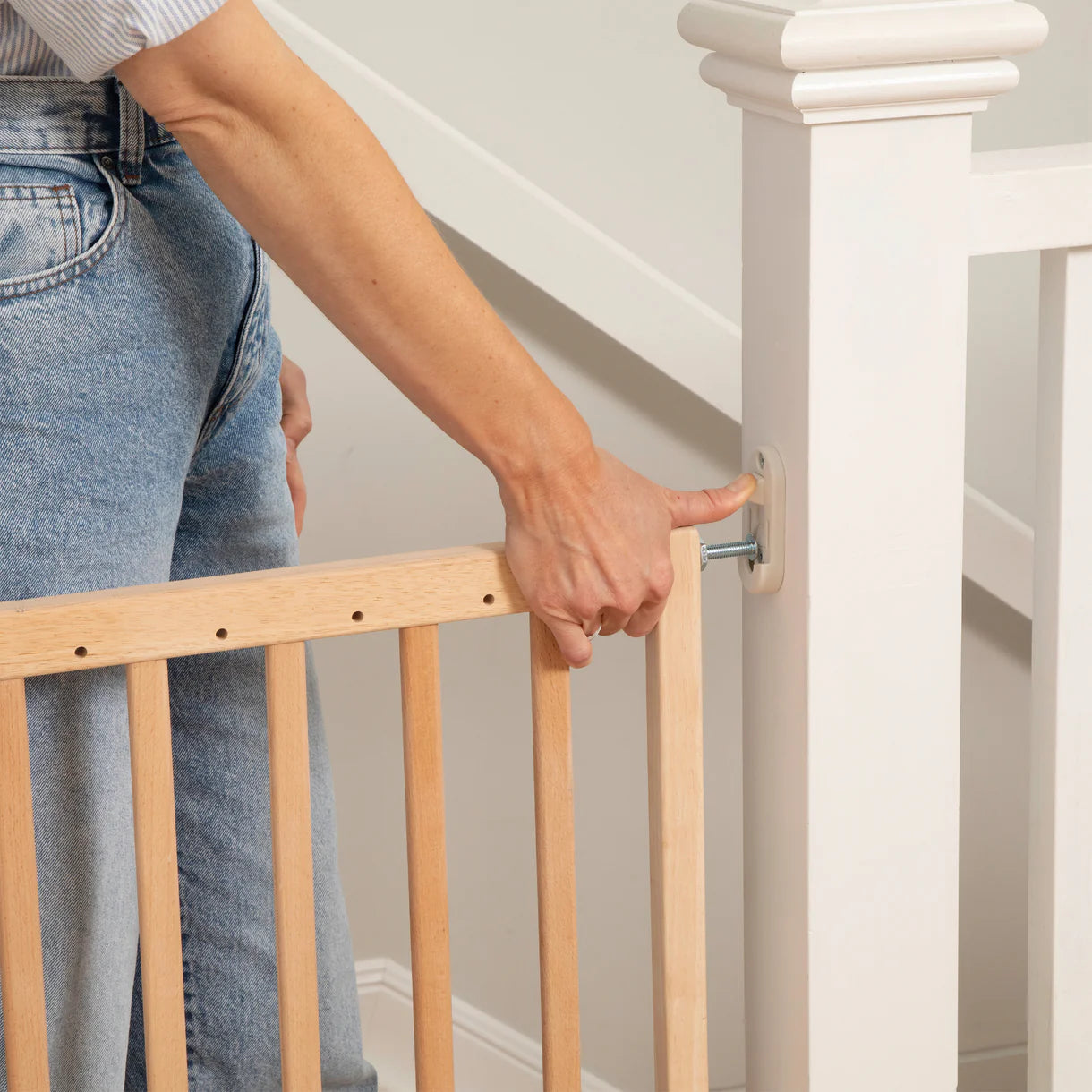Person adjusting a wooden stair gate on a staircase.