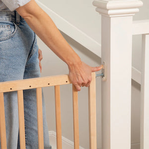 Person adjusting a wooden stair gate on a staircase.