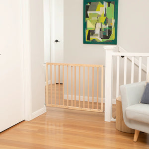 Wooden baby gate in a room with a white door, light-colored floor, and a piece of abstract art on the wall.