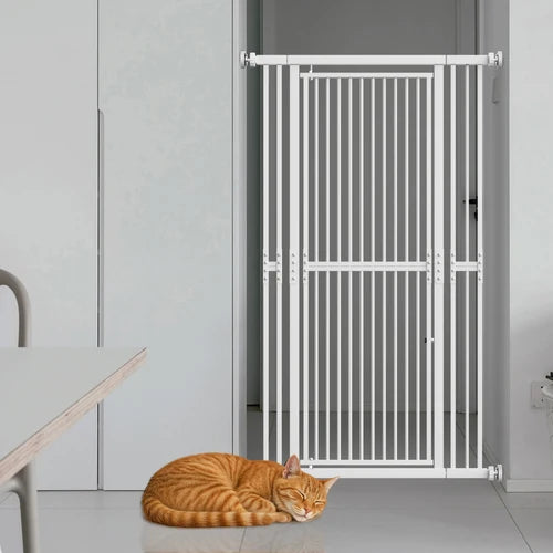A white metal pet gate installed in a doorway, with an orange tabby cat sleeping on the floor in front of it. The scene is set in a clean, modern room with light gray walls and a white table partially visible on the left at PET SERVO