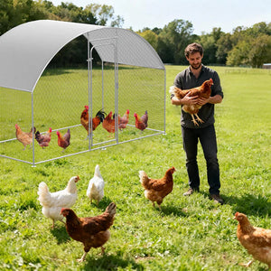 Man holding a chicken next to a portable chicken coop in an outdoor setting